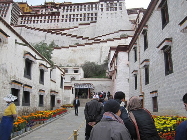 Du khách mặc áo lông vũ và khăn đa năng đứng trước Cung điện Potala buổi sáng sớm